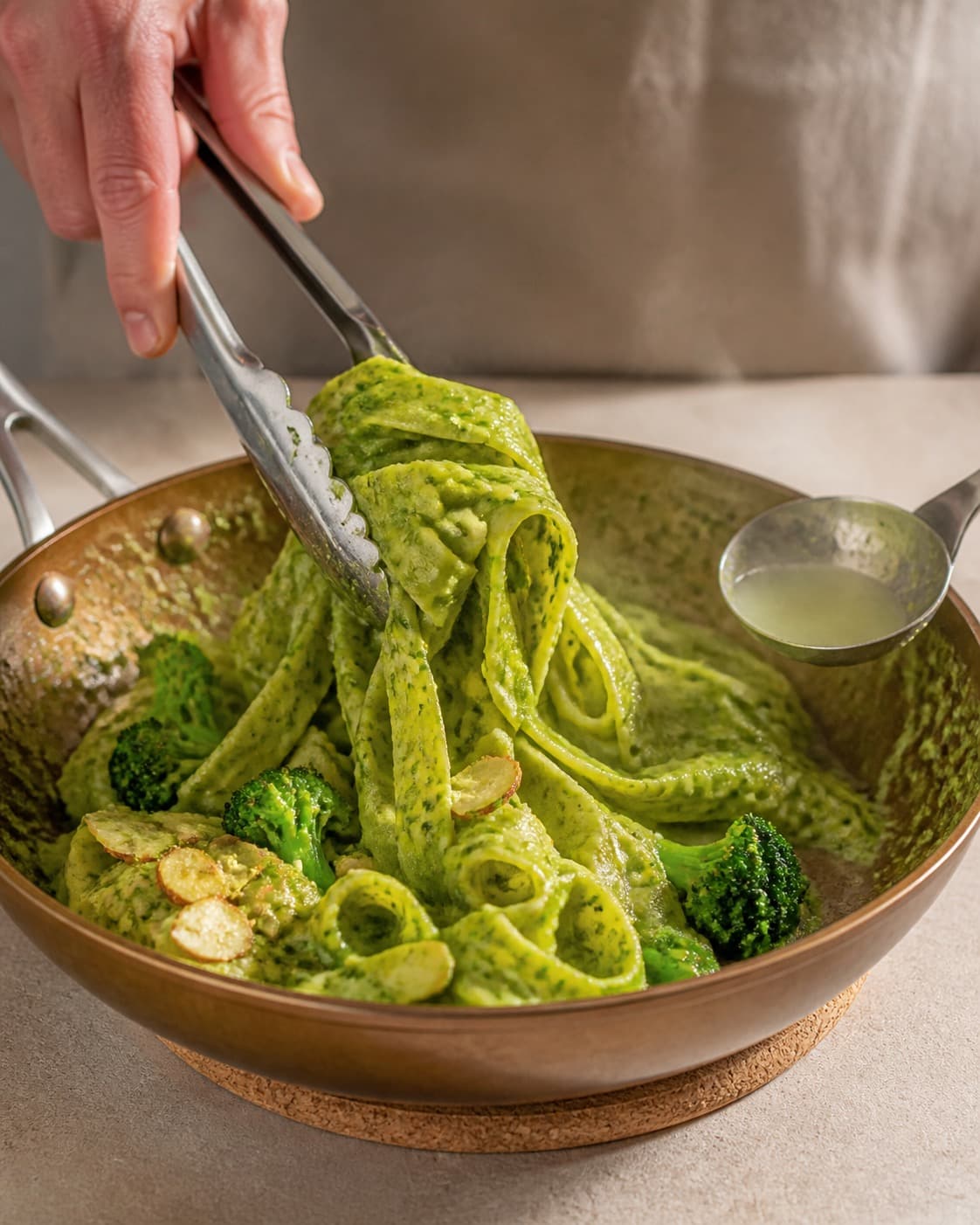 Pasta svinges blank med broccoli-basilikumpestoen og en smule pastavand under tilberedningen af pasta pesto med broccoli, mandel og citron