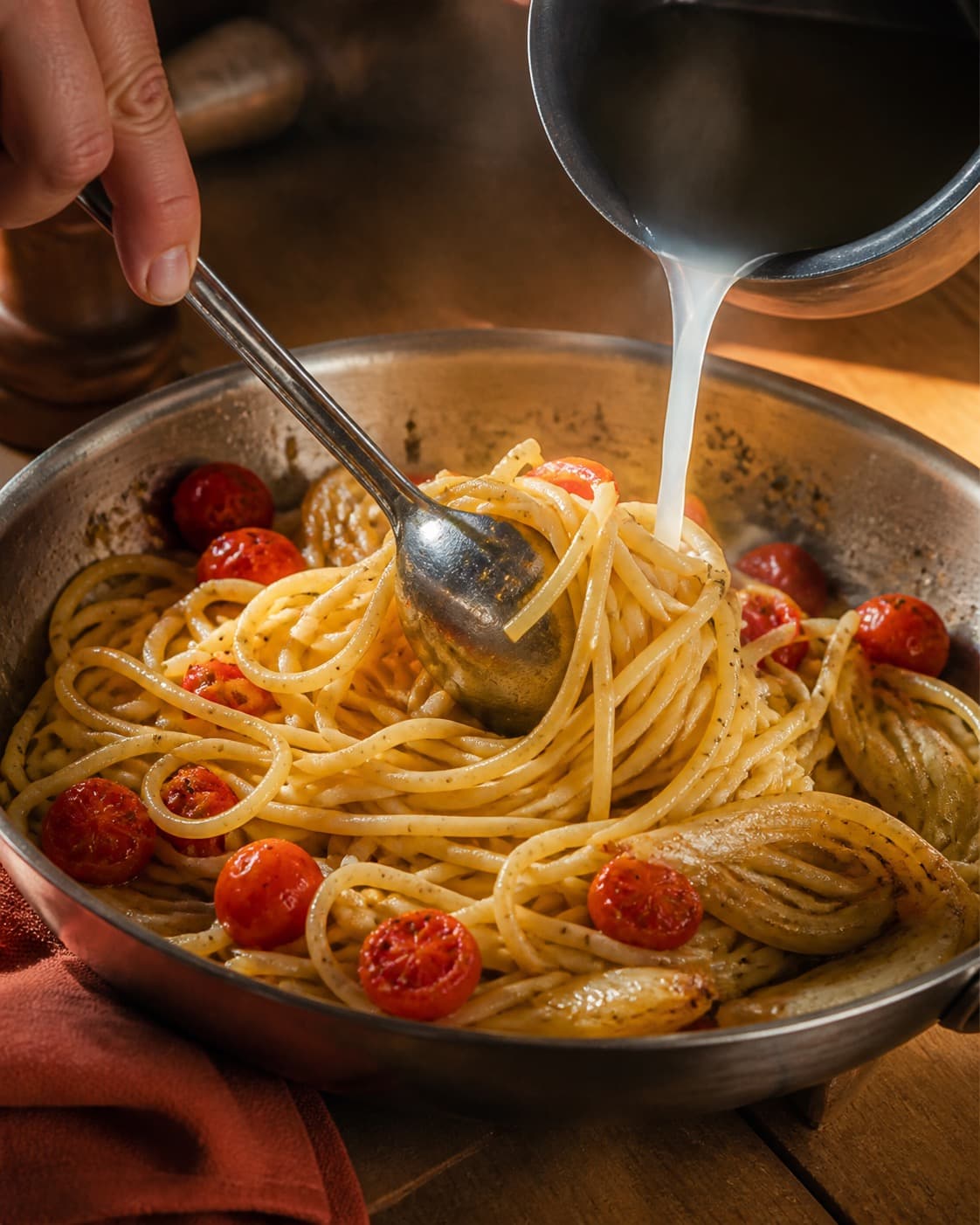 Pasta svinges blank med ovntomater og karamelliseret fennikel og en smule pastavand under tilberedningen af pasta med bagte tomater, burrata og fennikel