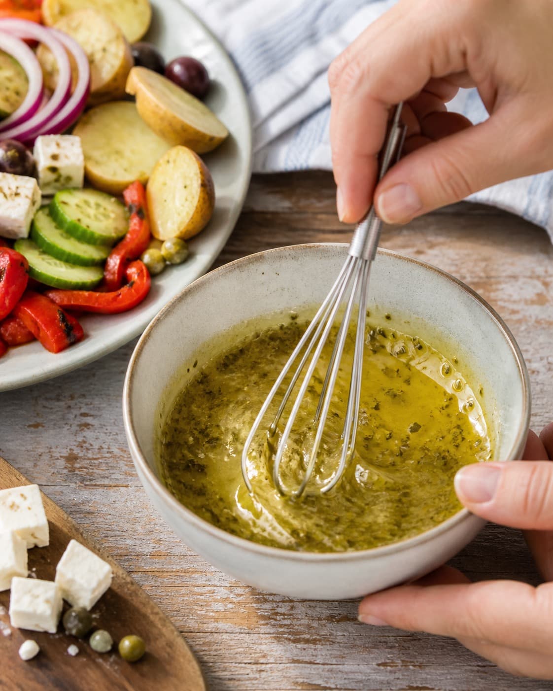 citron-oreganovinaigretten piskes blank i en lille skål under tilberedningen af græsk kartoffelsalat med feta, peberfrugt og kapers
