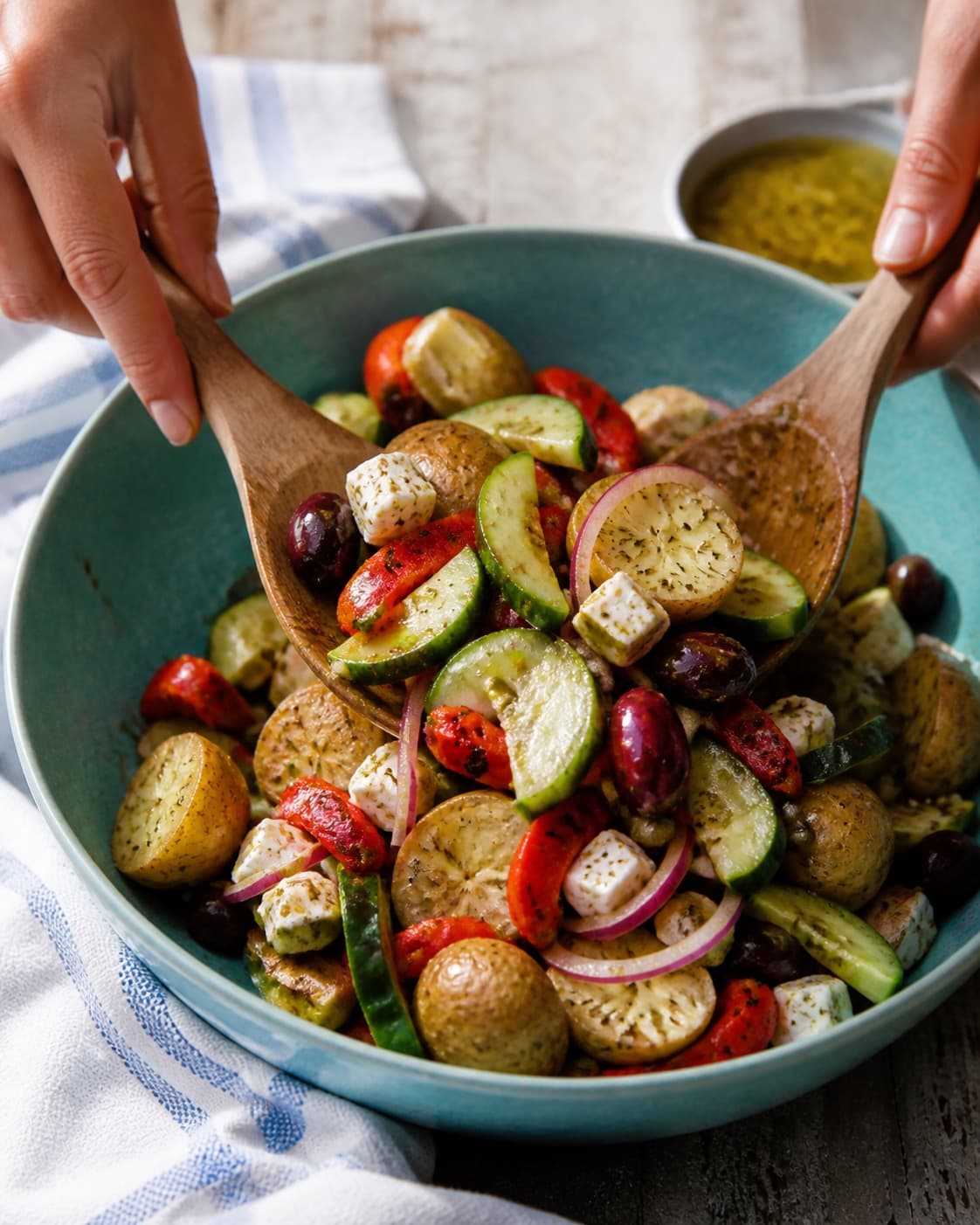 den græske kartoffelsalat vendes nænsomt med citron-oreganovinaigretten under tilberedningen af græsk kartoffelsalat med feta, peberfrugt og kapers