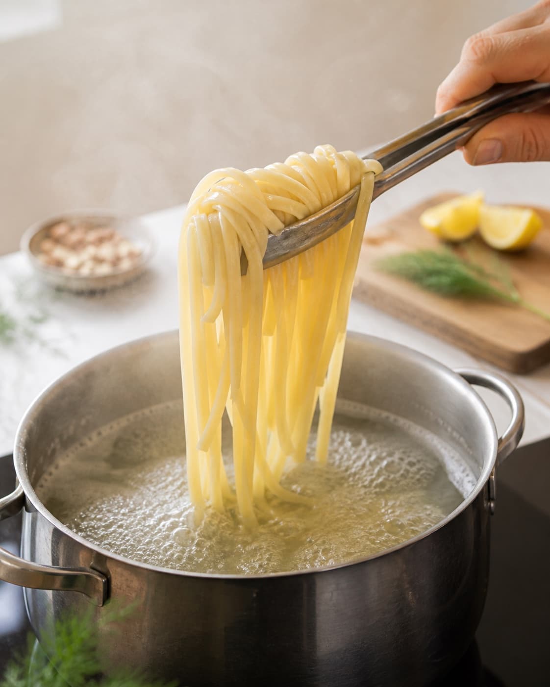 Pasta løftes fra boblende vand med fast kerne under tilberedningen af tagliatelle med varmrøget laks, dildpesto og citron