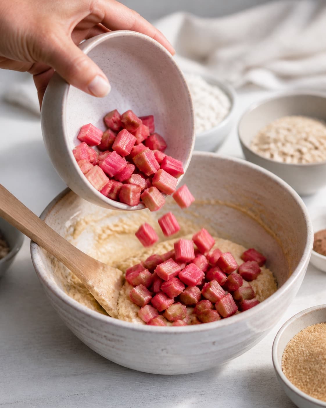 Afvejede råvarer til rabarbermuffinsene ligger adskilt i lyse skåle under tilberedningen af rabarbermuffins med marcipan, hvid chokolade og havrecrumble