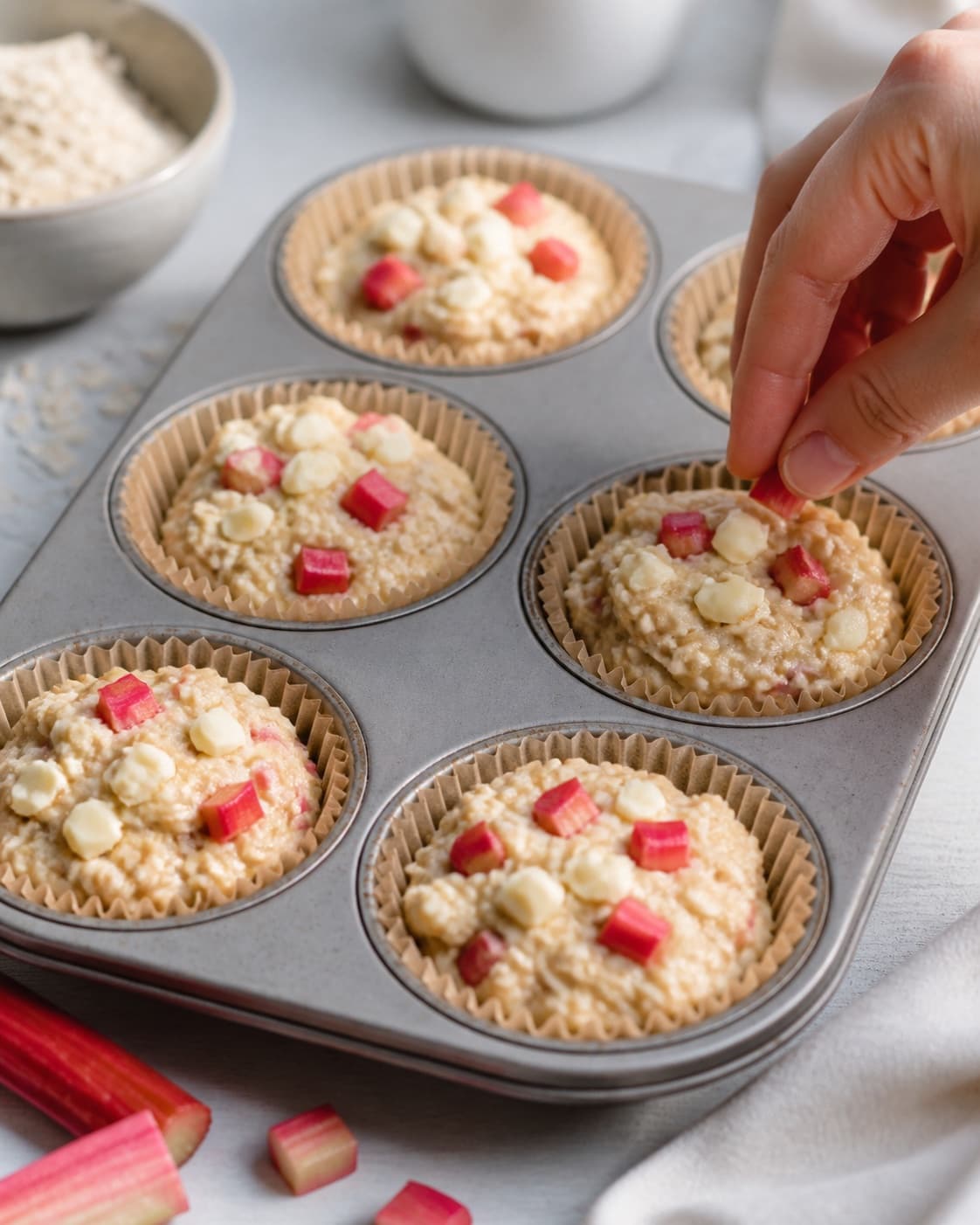 rabarber og hvid chokolade fordeles jævnt i den ubagte rabarbermuffinsene under tilberedningen af rabarbermuffins med marcipan, hvid chokolade og havrecrumble