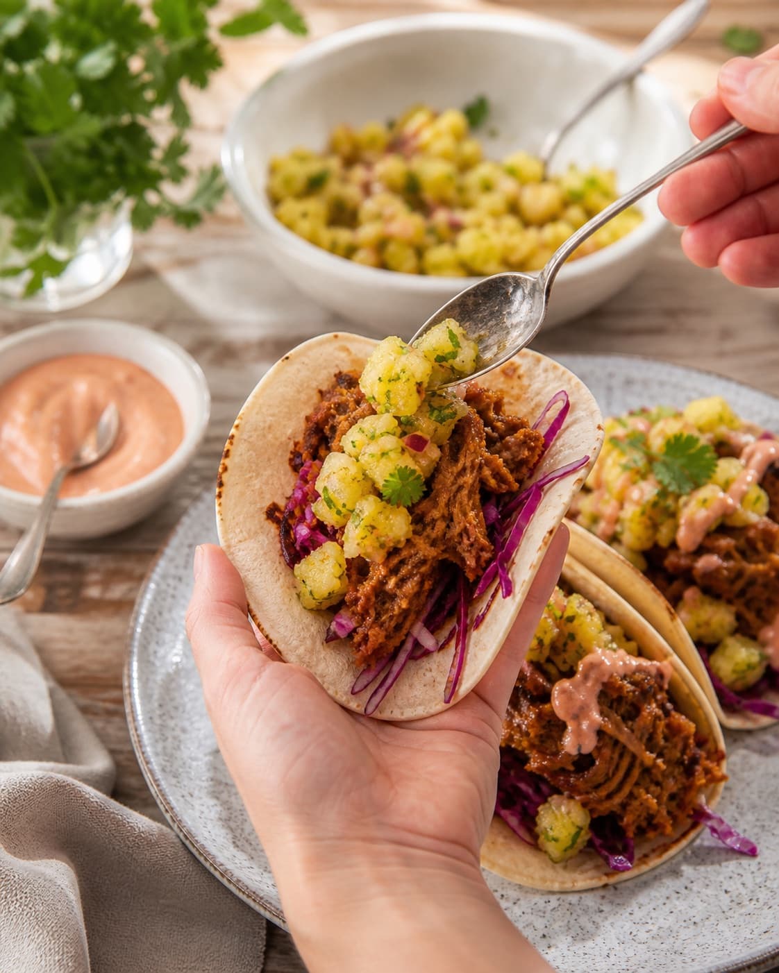 pulled pork-tacosene anrettes luftigt med koriander og varme majstortillas under tilberedningen af pulled pork-tacos med ananassalsa og chipotlecreme