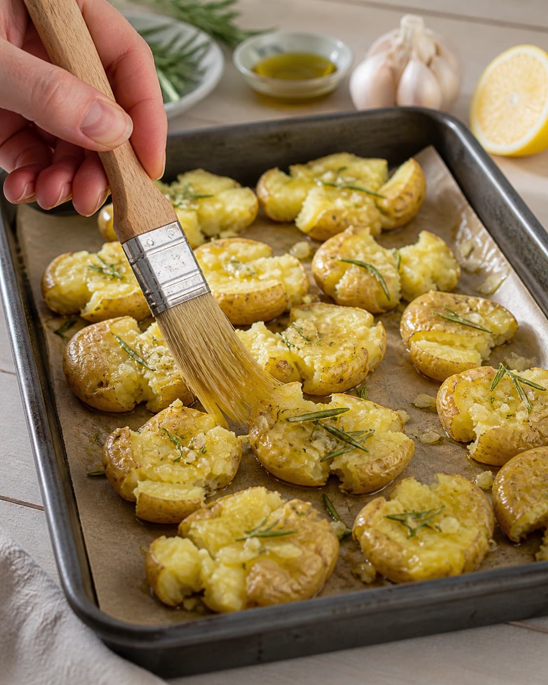 forkogte knuste kartofler pensles jævnt med olivenolie, hvidløg og rosmarin under tilberedningen af rosmarinkartofler med citron, hvidløg og parmesan