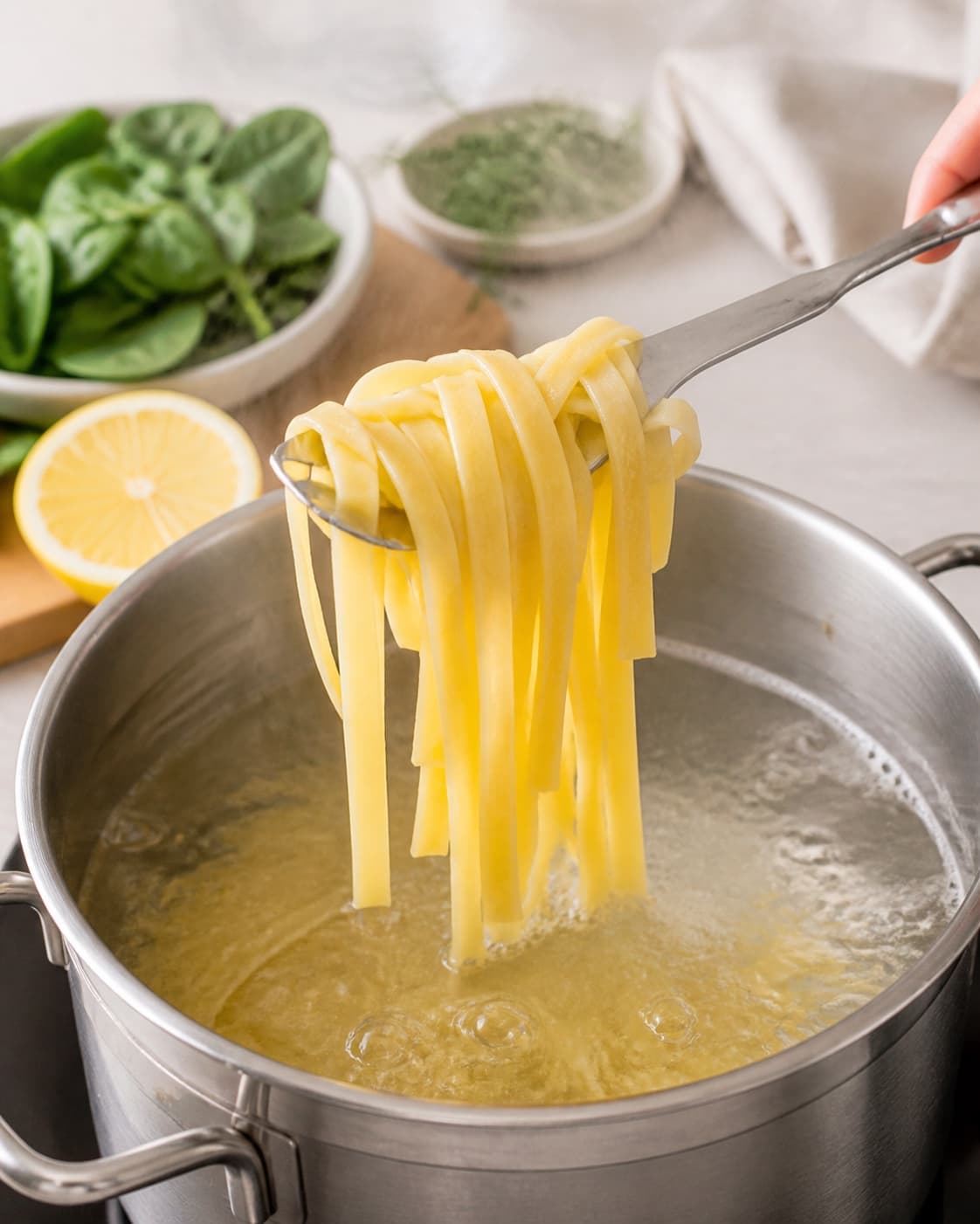 Pasta løftes fra boblende vand med fast kerne under tilberedningen af pasta med laks, spinat og citronflødesauce