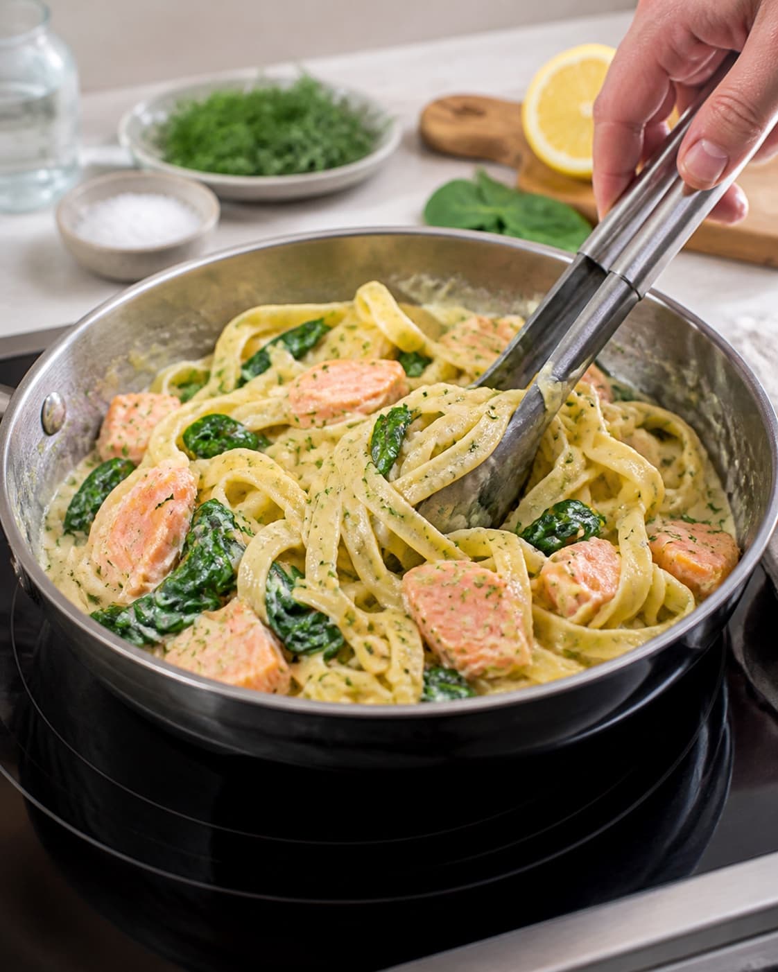 Pasta svinges blank med skalotteløg, spinat og citronfløde under tilberedningen af pasta med laks, spinat og citronflødesauce
