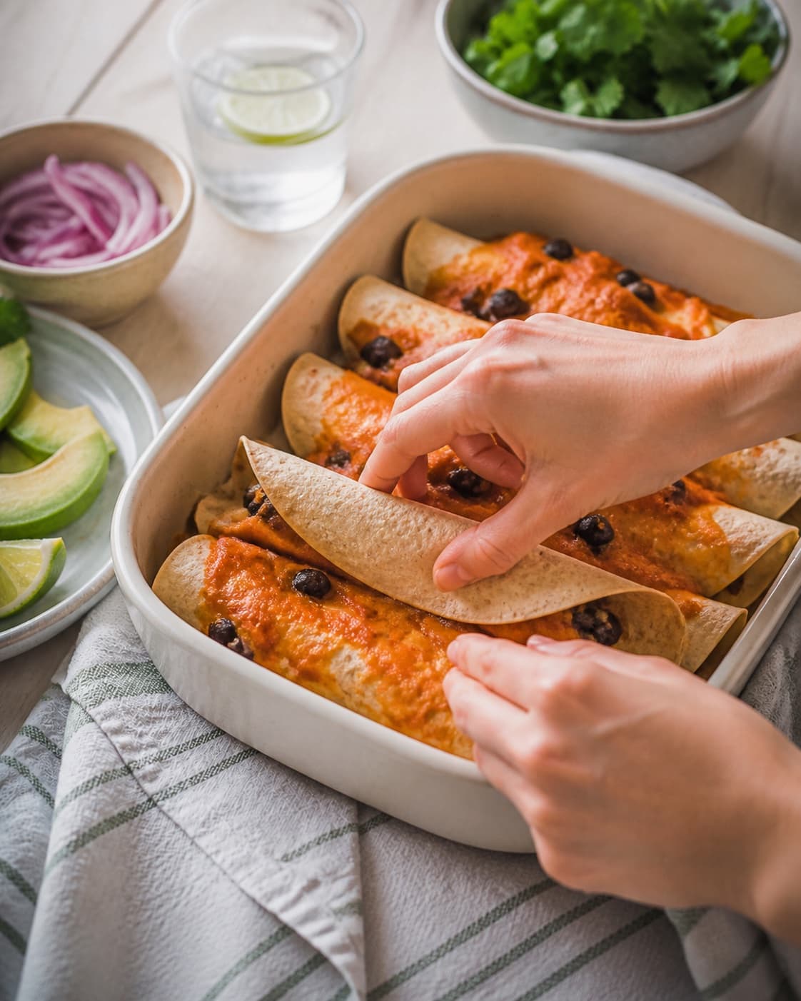 tortillas og røget tomatsauce samles nænsomt til okseenchiladaerne under tilberedningen af okseenchiladas med sorte bønner og røget tomatsauce