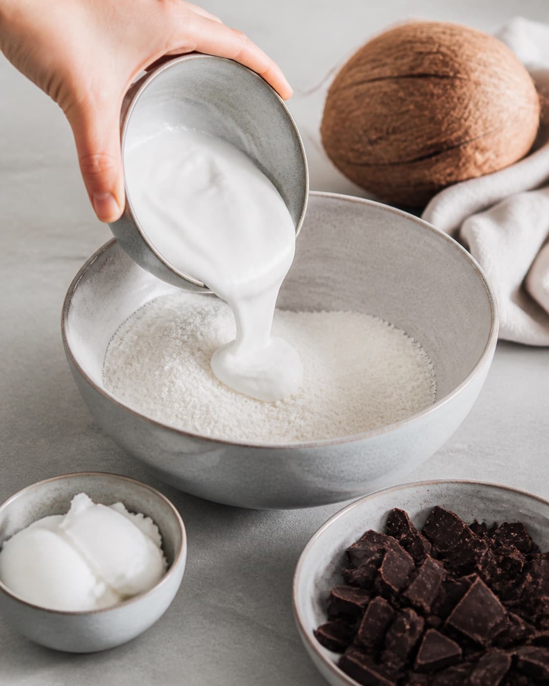 Measured ingredients for bountykugler arranged separately with kokosmel, mørk chokolade, kokosfløde, kokosolie under tilberedningen af bountykugler