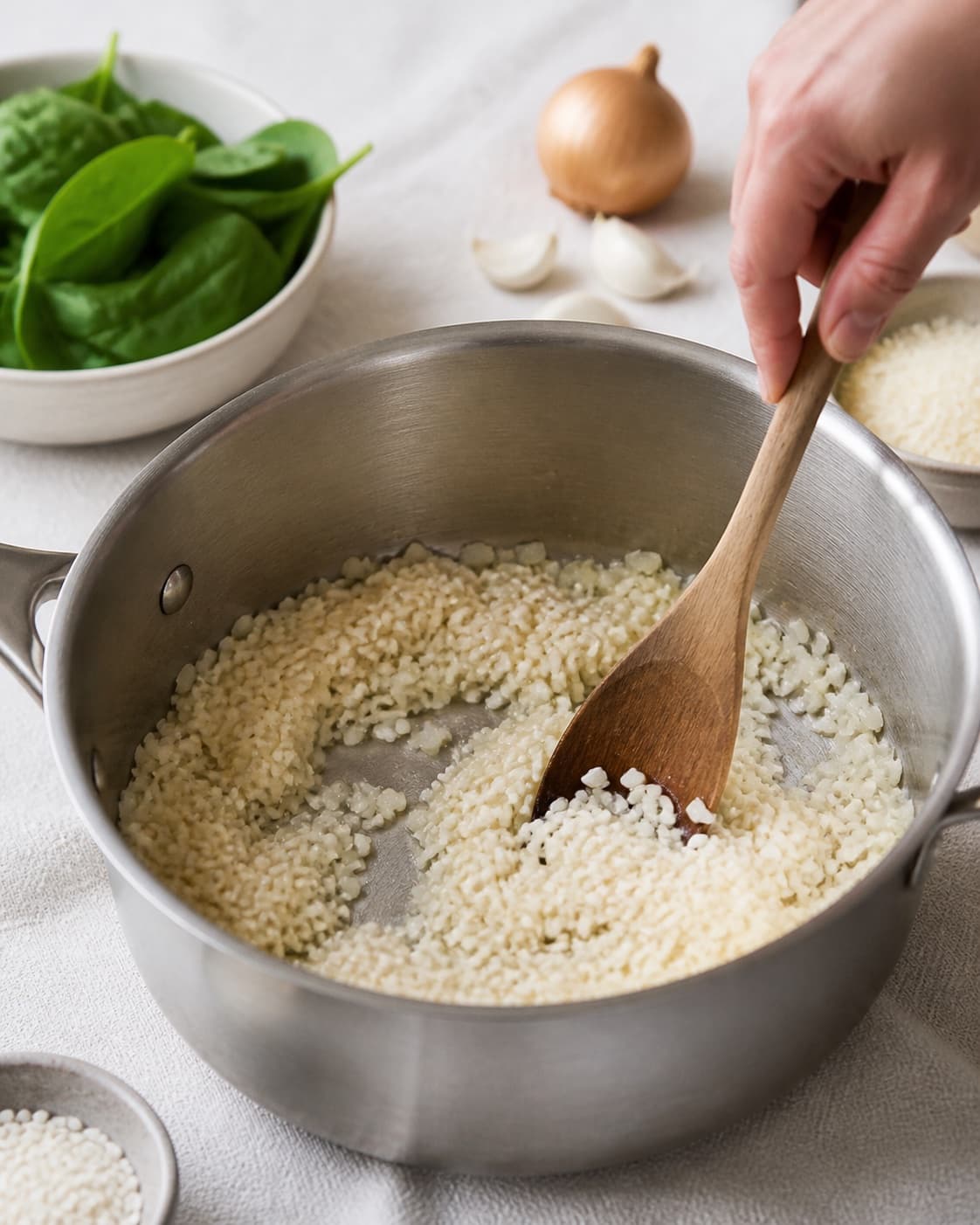 Mise en place for risotto med spinat with carnaroliris, frisk spinat, zittauerløg, hvidløg under tilberedningen af risotto med spinat
