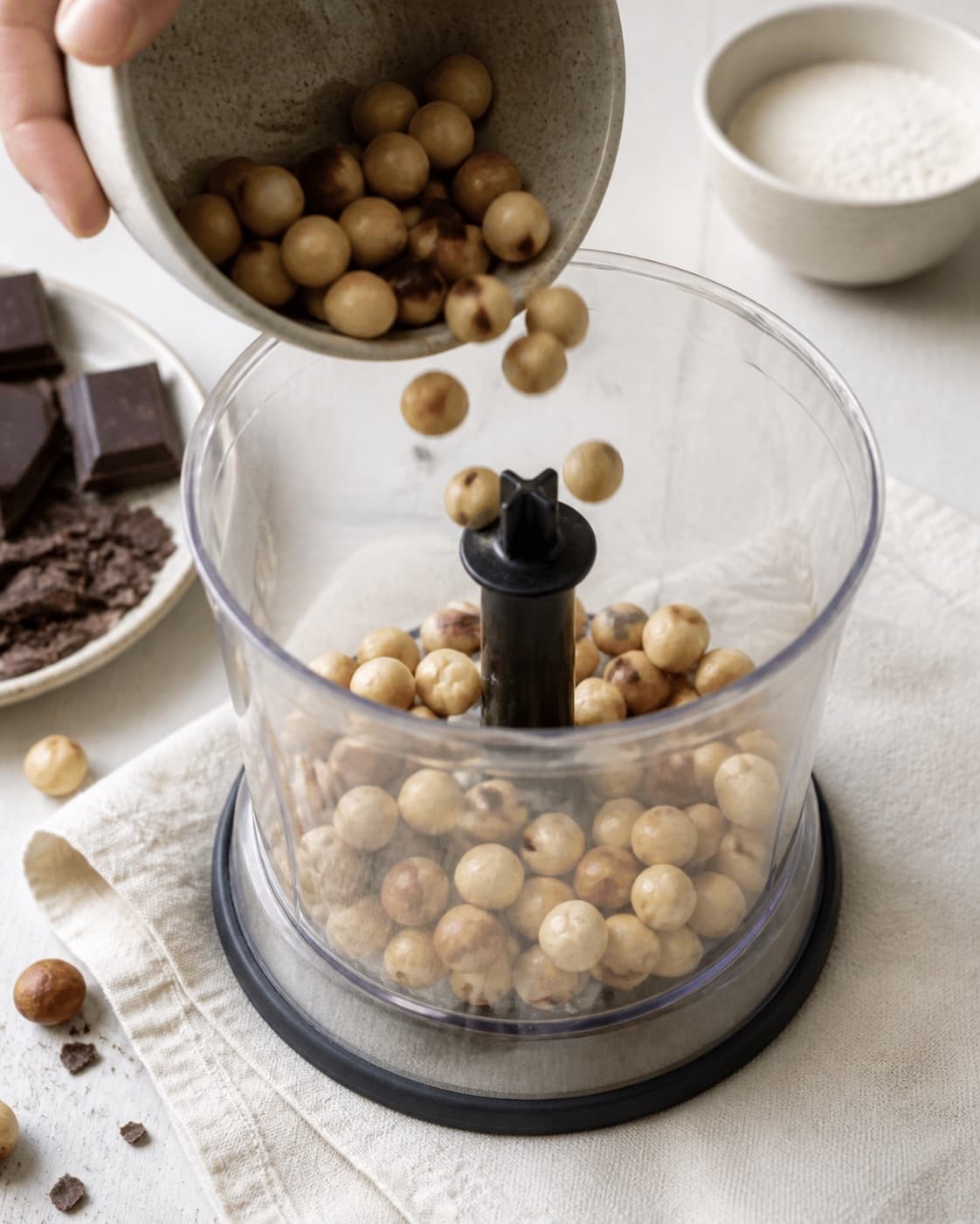 Measured ingredients for hasselnøddesmør med chokolade arranged separately with ristede hasselnødder, mørk chokolade, hasselnødder, hvedemel under tilberedningen af hasselnøddesmør med chokolade