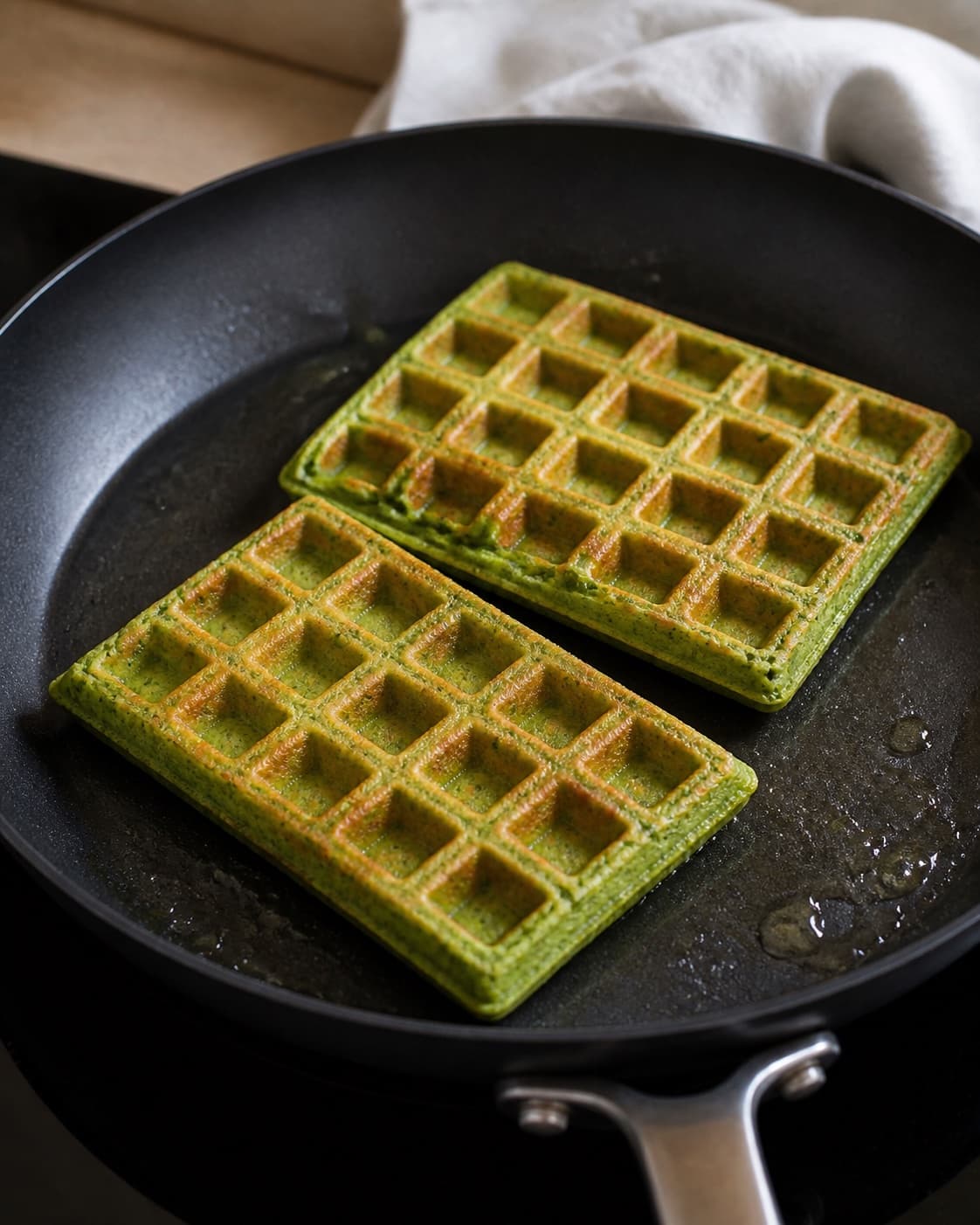 spinatvafler med røget laks og avocado frying to an even golden crust in a pan under tilberedningen af spinatvafler med røget laks og avocado