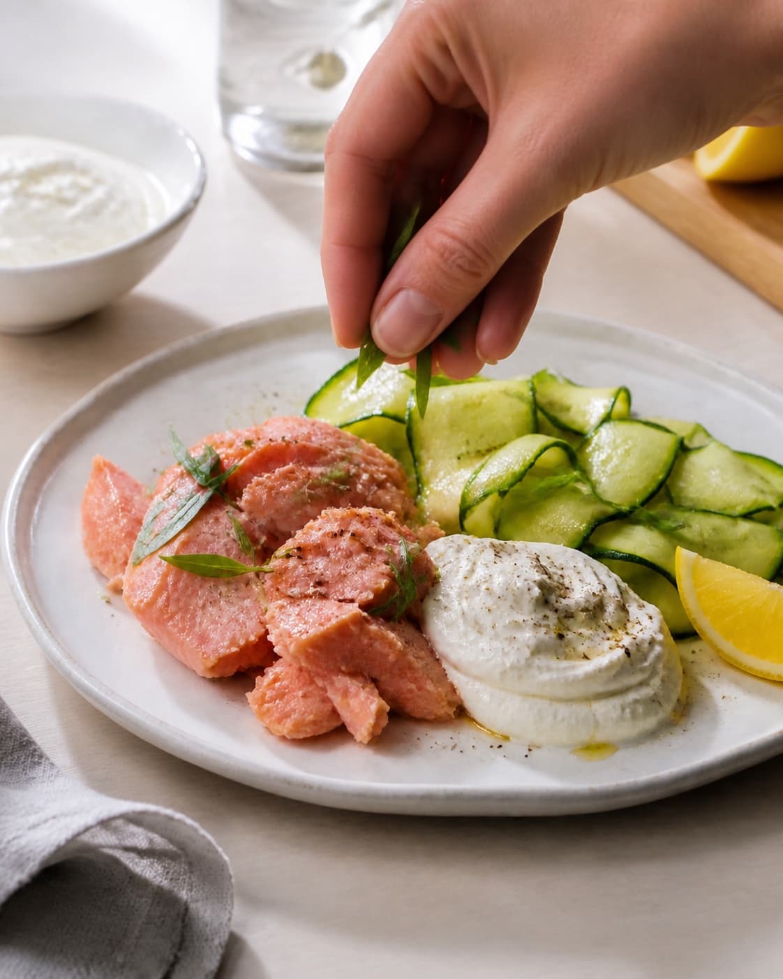 Fresh finished varmrøget laks med rygeostcreme og squashsalat receiving its final garnish under tilberedningen af varmrøget laks med rygeostcreme og squashsalat
