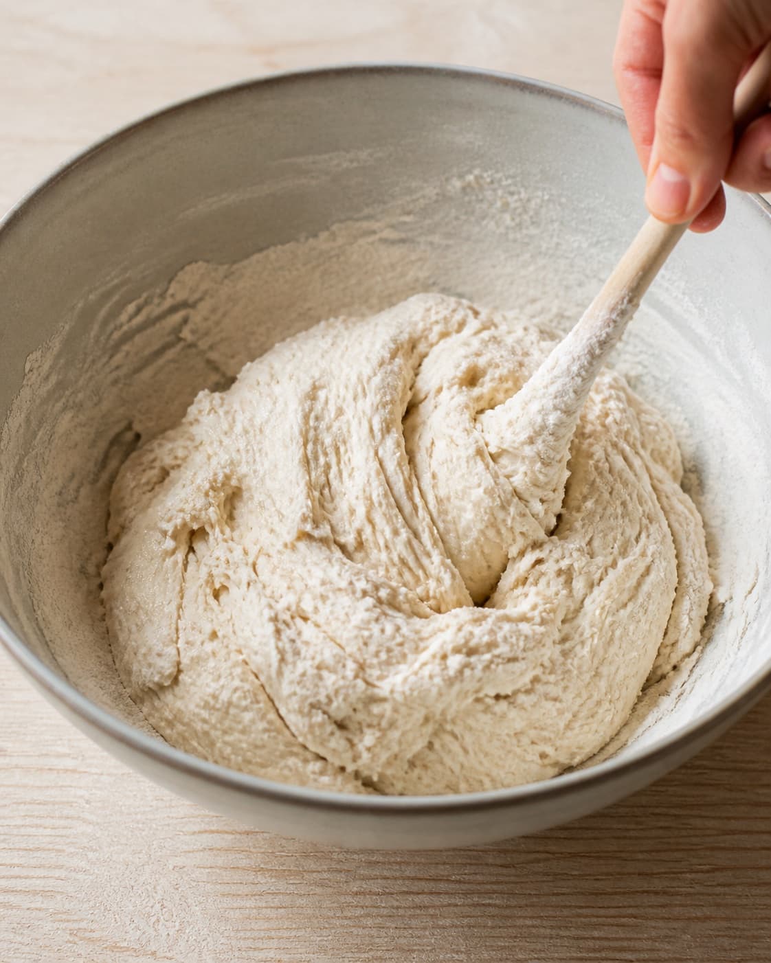 Close view of the moist dough for hjemmebagte luftige boller being mixed in a bowl with hvedemel, lunkent vand, gær, fint salt under tilberedningen af hjemmebagte luftige boller