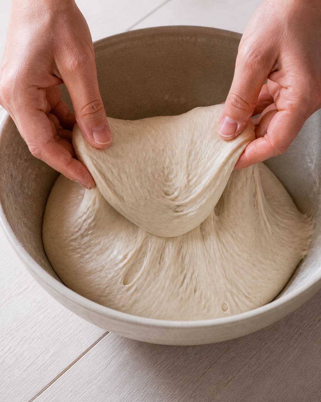 Hands gently folding elastic dough for grydebrød med surdej under tilberedningen af grydebrød med surdej