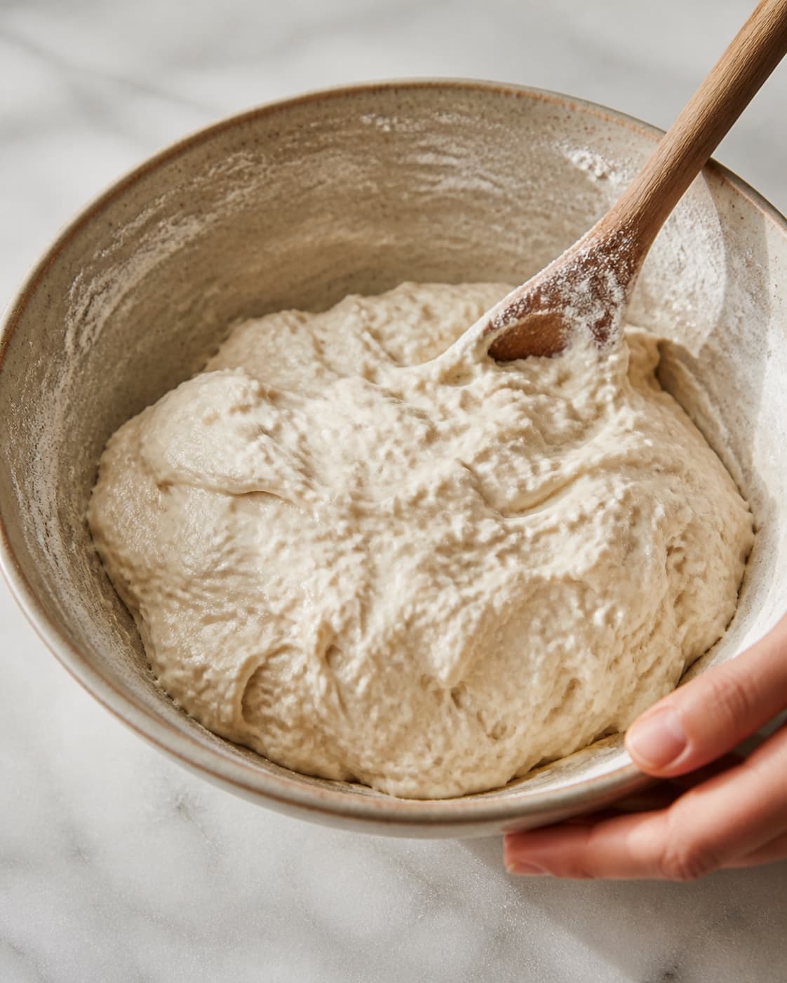 Close view of the moist dough for pandebrød med gær being mixed in a bowl with hvedemel, lunkent vand, gær, fint salt under tilberedningen af pandebrød med gær