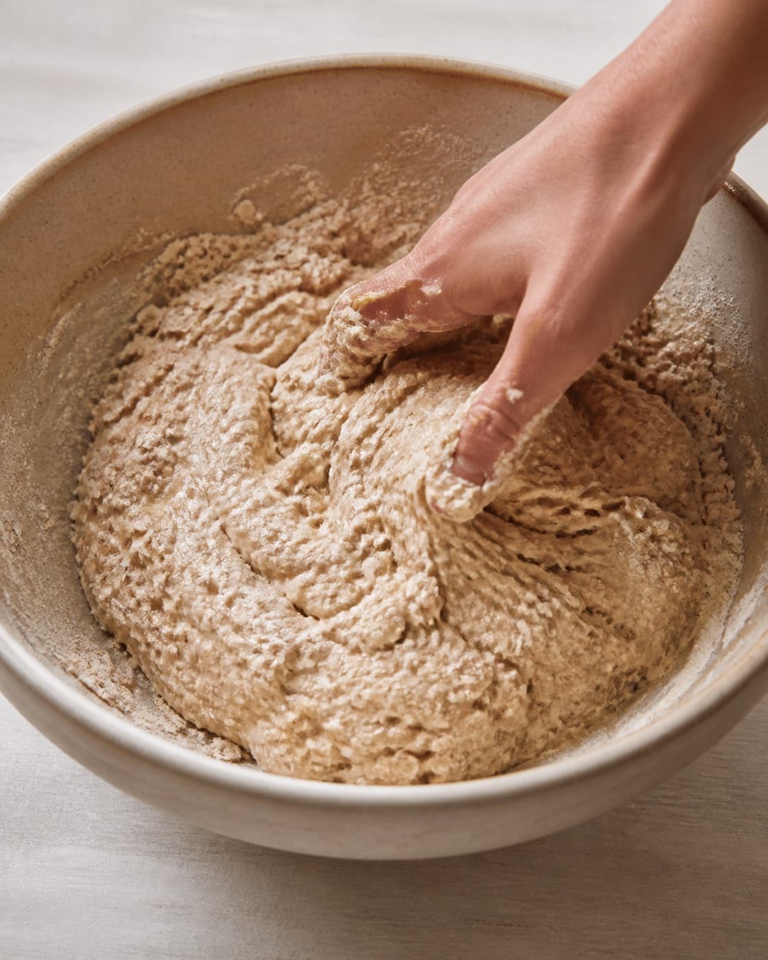 Close view of the moist dough for koldhævede surdejsboller med rugmel og havre being mixed in a bowl with rugmel, havregryn, aktiv surdej, hvedemel under tilberedningen af koldhævede surdejsboller med rugmel og havre