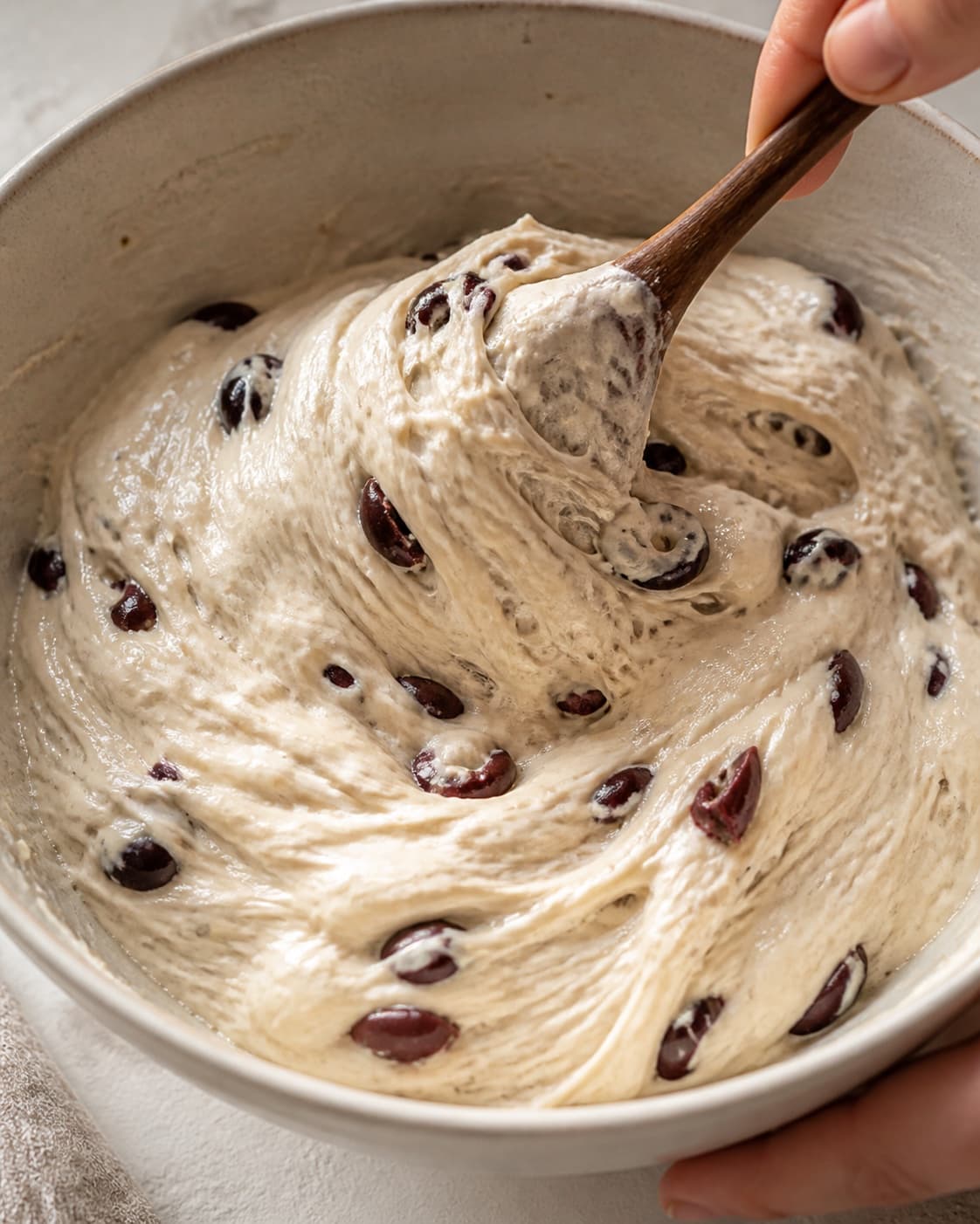 Close view of the moist dough for foccacia med surdej og oliven being mixed in a bowl with kalamataoliven, aktiv surdej, olivenolie, hvedemel under tilberedningen af foccacia med surdej og oliven