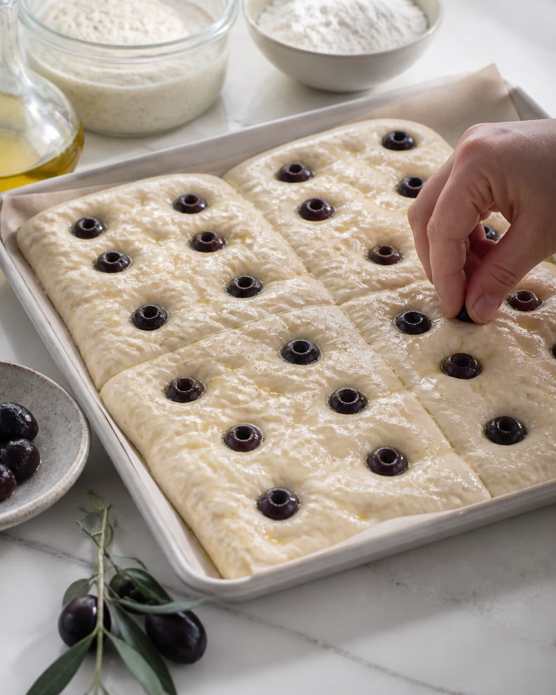 Even pieces of foccacia med surdej og oliven being shaped before baking under tilberedningen af foccacia med surdej og oliven