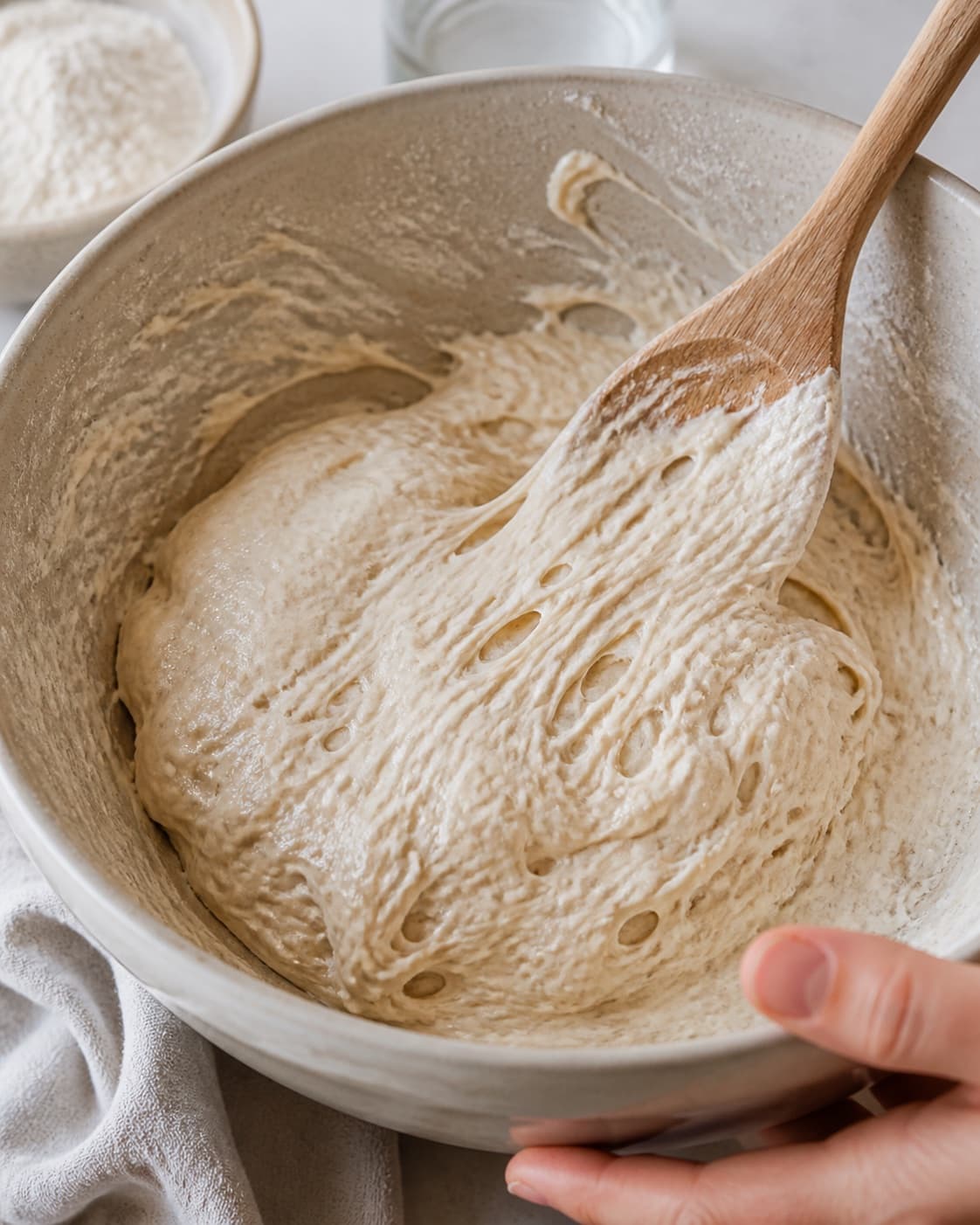 Close view of the moist dough for ciabattaboller med surdej being mixed in a bowl with aktiv surdej, hvedemel, lunkent vand, gær under tilberedningen af ciabattaboller med surdej