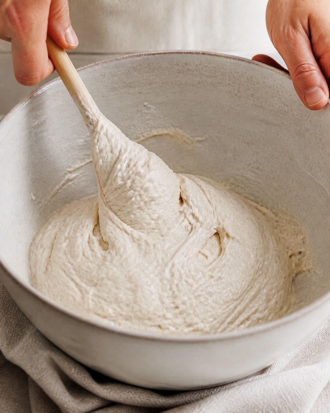 Close view of the moist dough for surdejsbrød med autolyse being mixed in a bowl with aktiv surdej, hvedemel, lunkent vand, gær under tilberedningen af surdejsbrød med autolyse