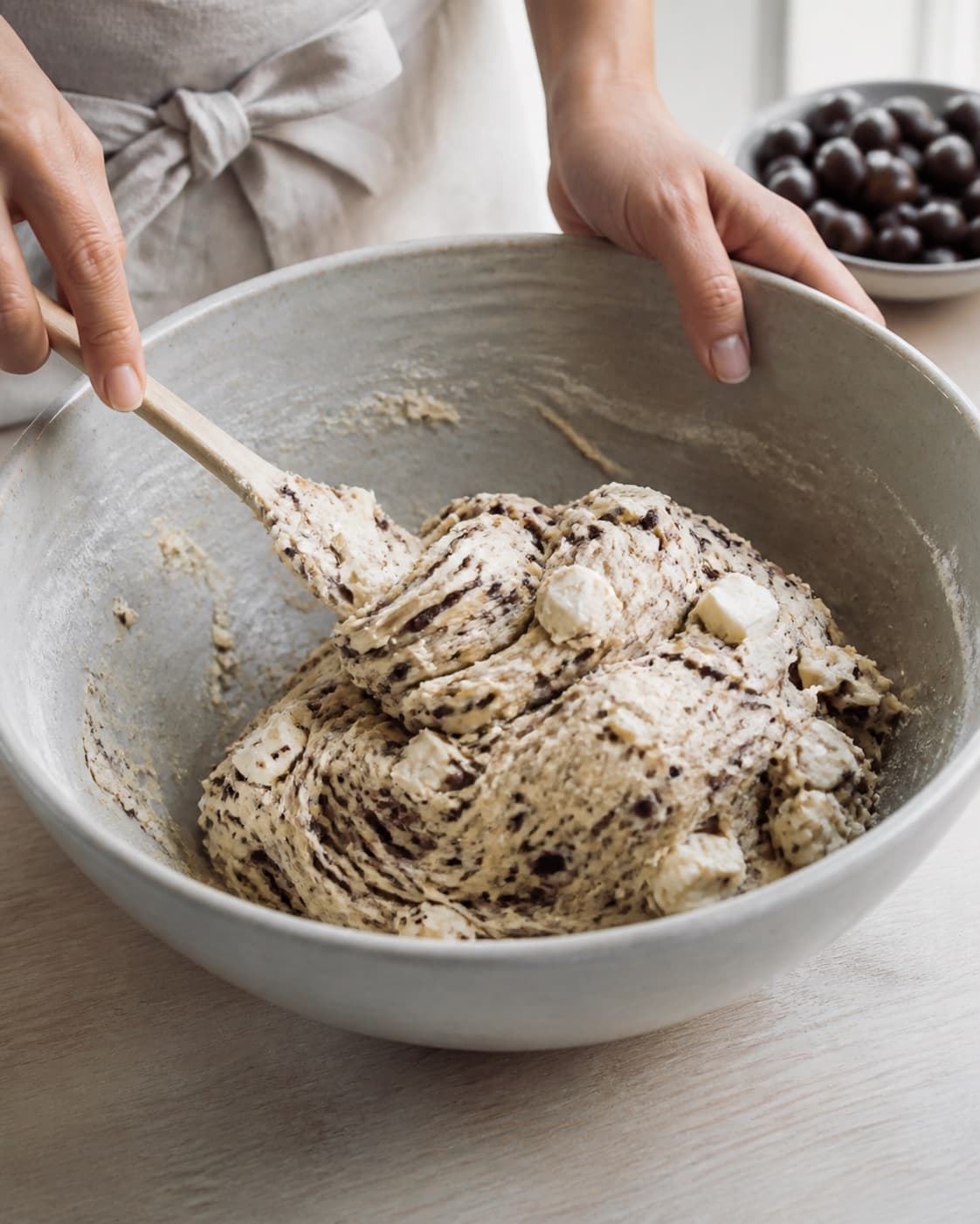 Close view of the moist dough for flettet brød med oliventapenade og feta being mixed in a bowl with oliventapenade, feta, hvedemel, lunkent vand under tilberedningen af flettet brød med oliventapenade og feta