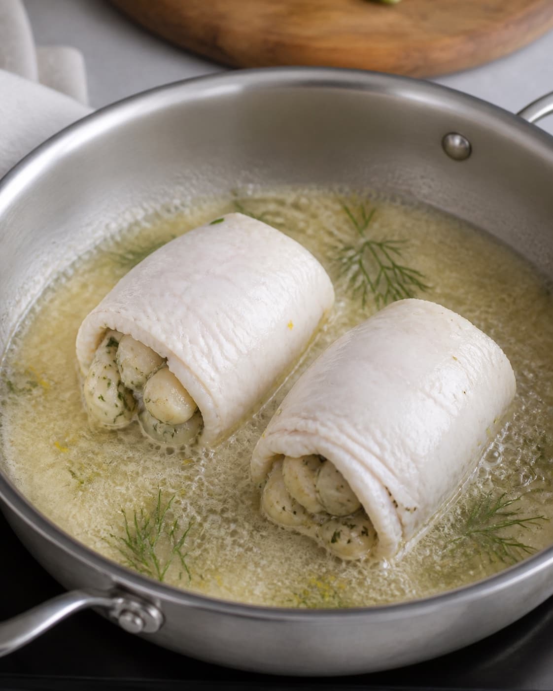 farserede rødspætter med fyld af kammusling gently simmering with visible ingredients under tilberedningen af farserede rødspætter med fyld af kammusling