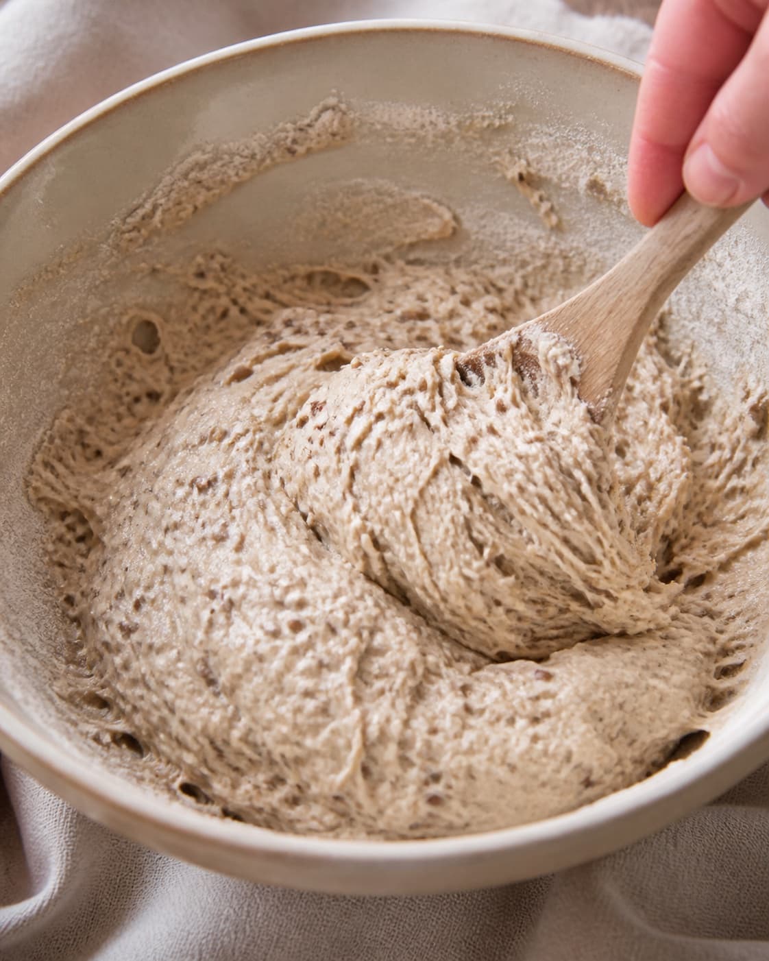 Close view of the moist dough for koldhævede kerneboller being mixed in a bowl with hvedemel, lunkent vand, gær, fint salt under tilberedningen af koldhævede kerneboller