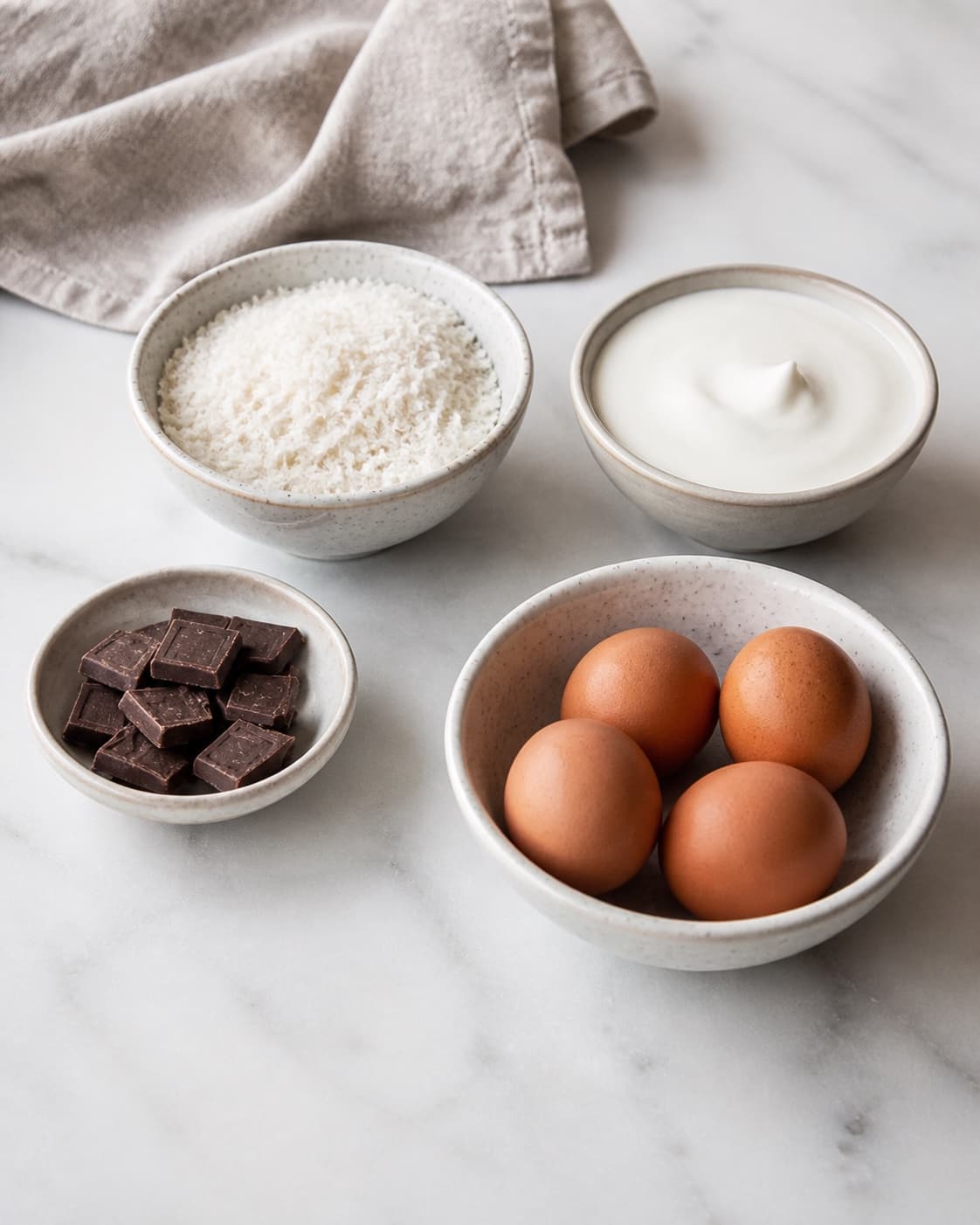 Measured ingredients for bountykage uden mel og sukker arranged separately with kokosmel, mørk chokolade, kokosfløde, æg under tilberedningen af bountykage uden mel og sukker