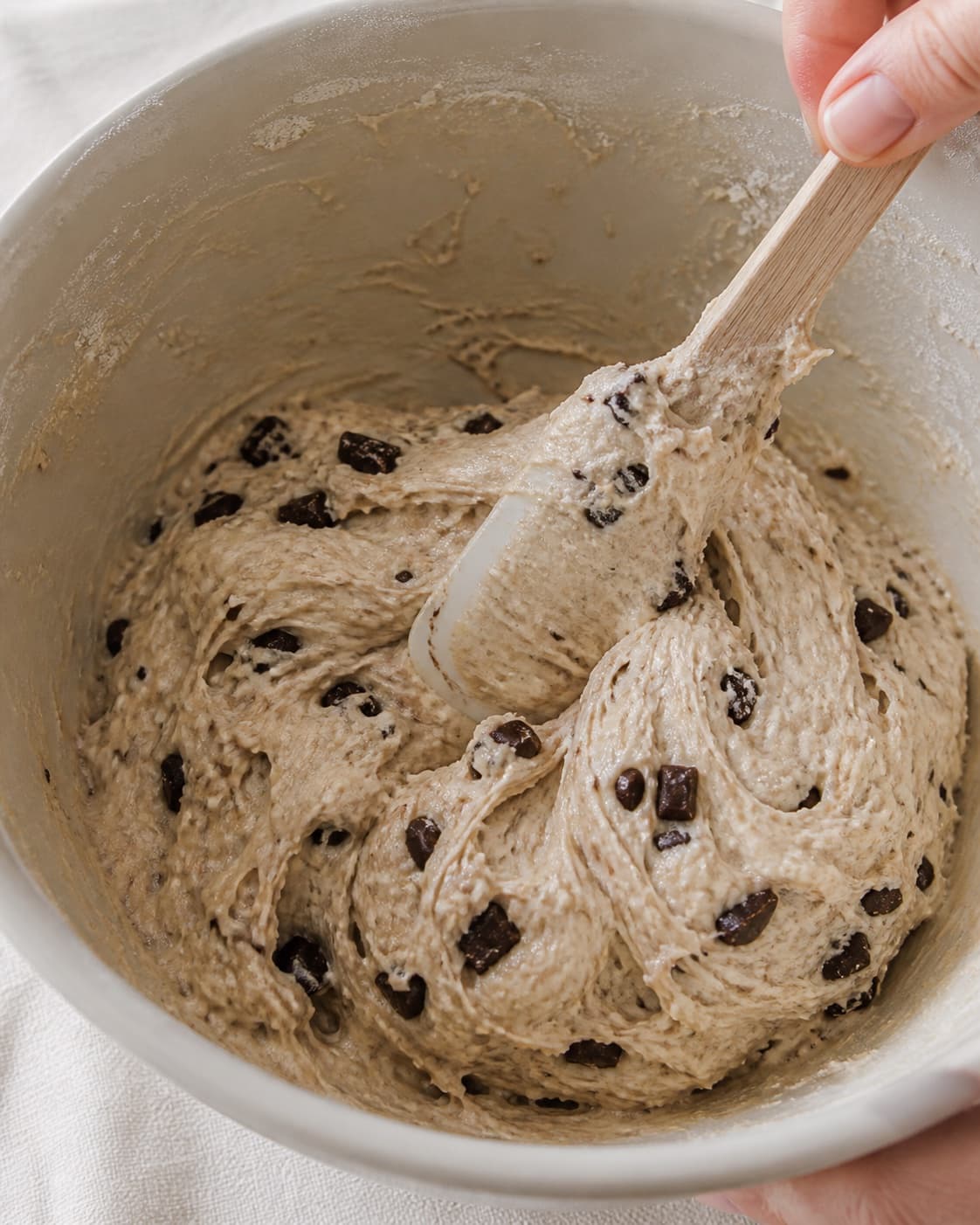 Close view of the moist dough for chokoladeboller med surdej being mixed in a bowl with aktiv surdej, mørk chokolade, hvedemel, lunkent vand under tilberedningen af chokoladeboller med surdej