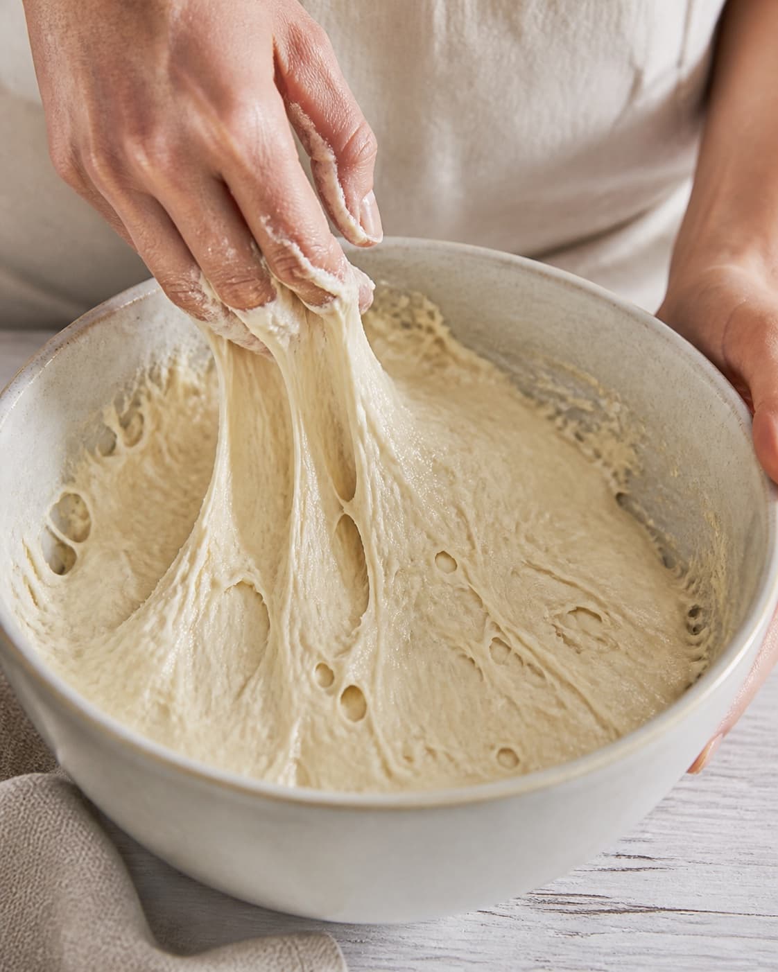 Close view of the moist dough for mini foccaciabrød med mozzarella og tomat being mixed in a bowl with mozzarella, modne tomater, olivenolie, hvedemel under tilberedningen af mini foccaciabrød med mozzarella og tomat