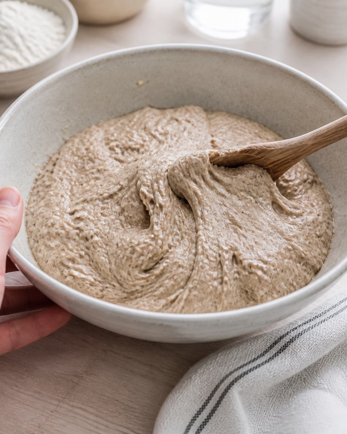 Close view of the moist dough for koldhævede speltboller being mixed in a bowl with fuldkornsspeltmel, hvedemel, lunkent vand, gær under tilberedningen af koldhævede speltboller