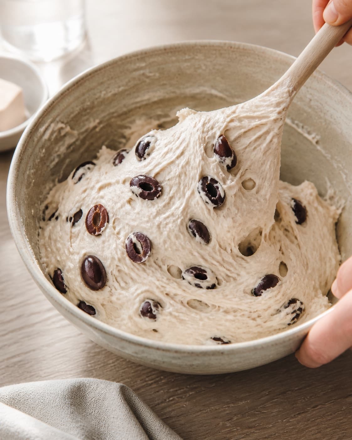 Close view of the moist dough for olivenbrød bagt i gryde being mixed in a bowl with hvedemel, lunkent vand, gær, kalamataoliven under tilberedningen af olivenbrød bagt i gryde