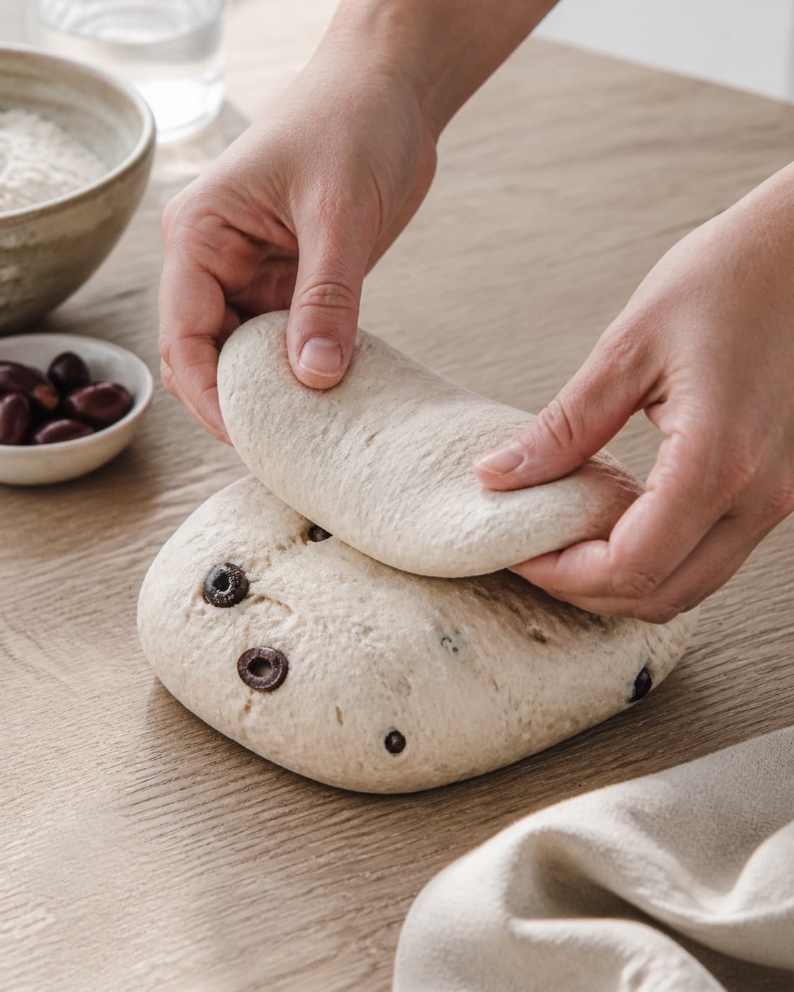 Hands gently folding elastic dough for olivenbrød bagt i gryde under tilberedningen af olivenbrød bagt i gryde