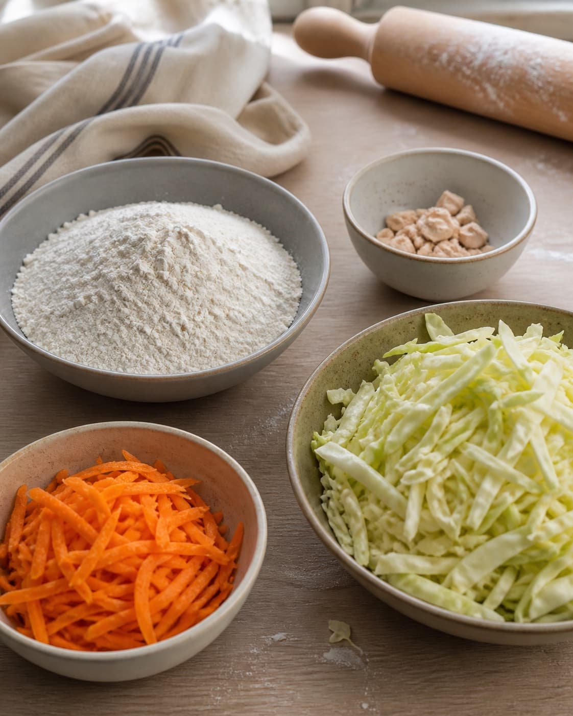 Measured ingredients for vegetariske pirogger med kål arranged separately with hvedemel, gær, hvidkål, gulerødder under tilberedningen af vegetariske pirogger med kål