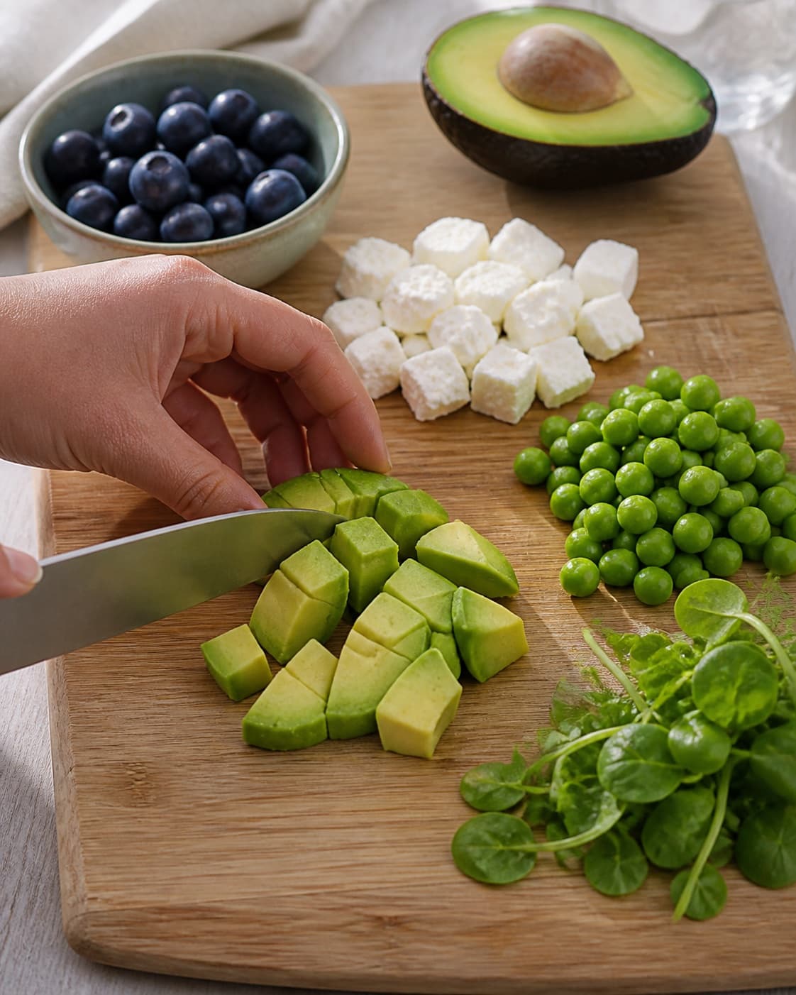 Ingredients for salat med blåbær, feta, ærter og avocado being cut into even pieces under tilberedningen af salat med blåbær, feta, ærter og avocado