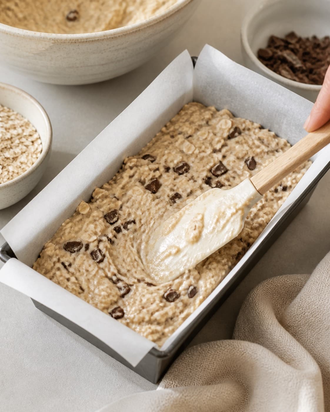 Banana cake batter with oats and chopped chocolate being folded and levelled in the tin under tilberedningen af sund banankage med chokolade