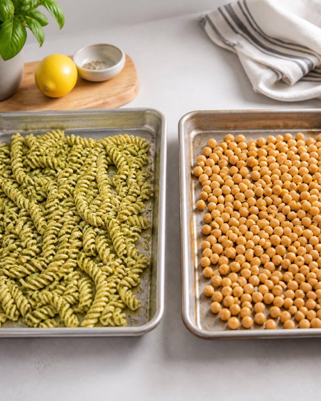 Dressed fusilli and drained chickpeas spread separately in thin layers to cool quickly under tilberedningen af pastasalat med kikærter, feta og pesto