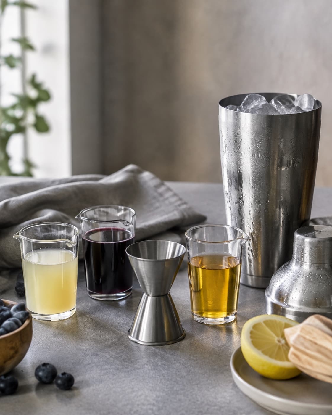 Afmålt gin, citron, blå appelsinlikør og blåbærsirup ved en tom shaker
