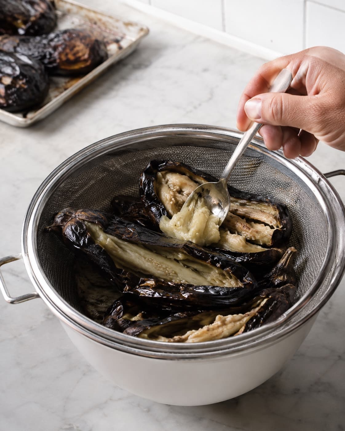 Blød røget aubergine skrabes fri af sort skind og drypper af i en si