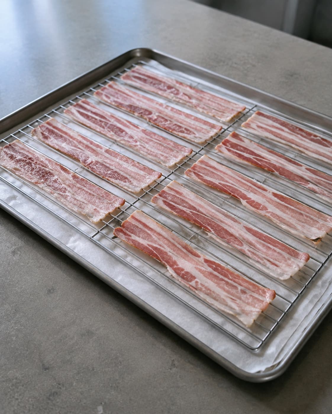 Rå baconskiver ligger uden overlap på metalrist over en foret bageplade