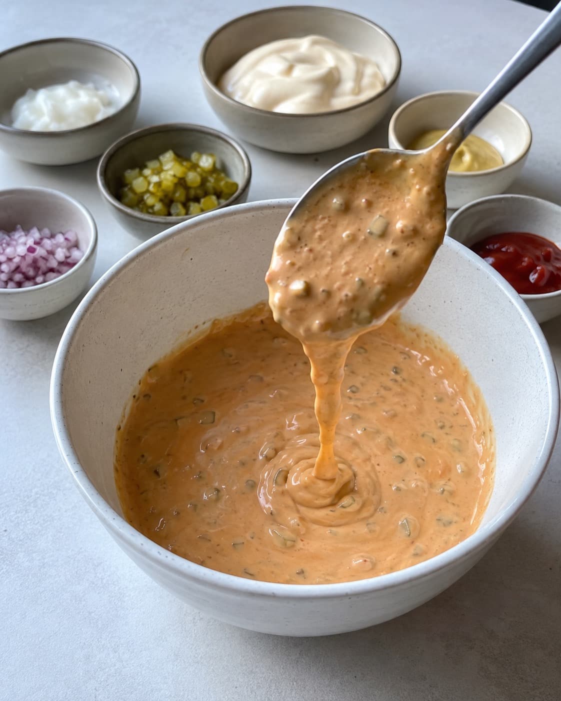 Tyk lys orange picklesauce med fine agurke- og løgstykker falder i bånd fra en ske