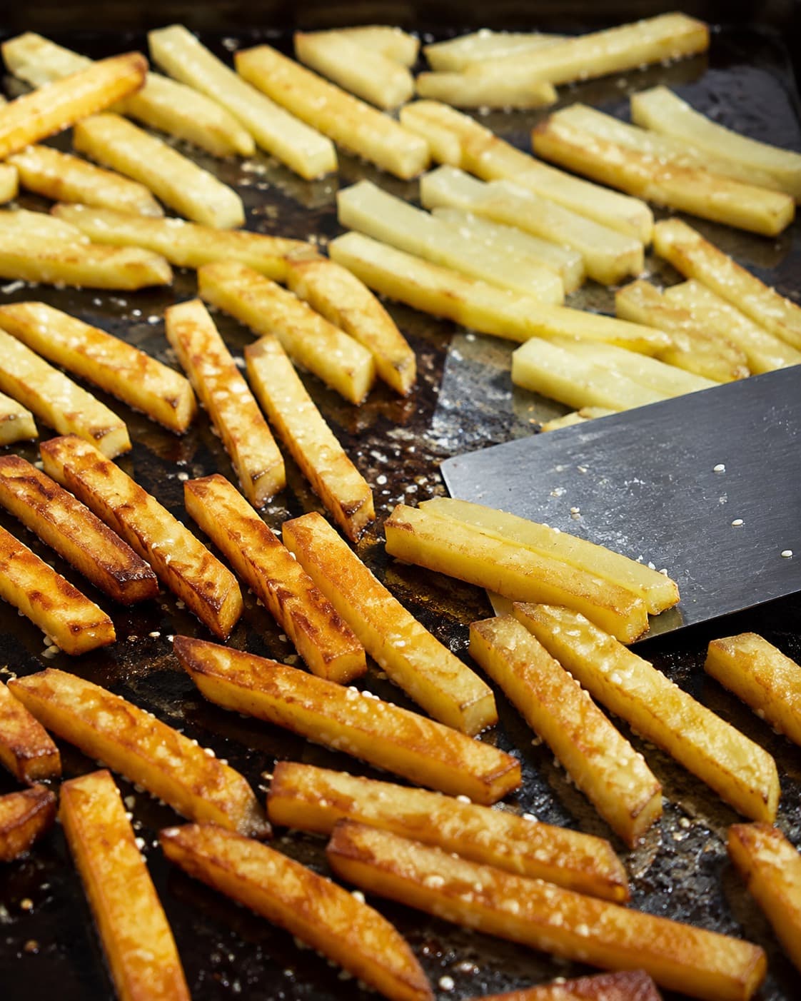 Ensartede kartoffelfritter med sesam vendes på en varm metalbageplade