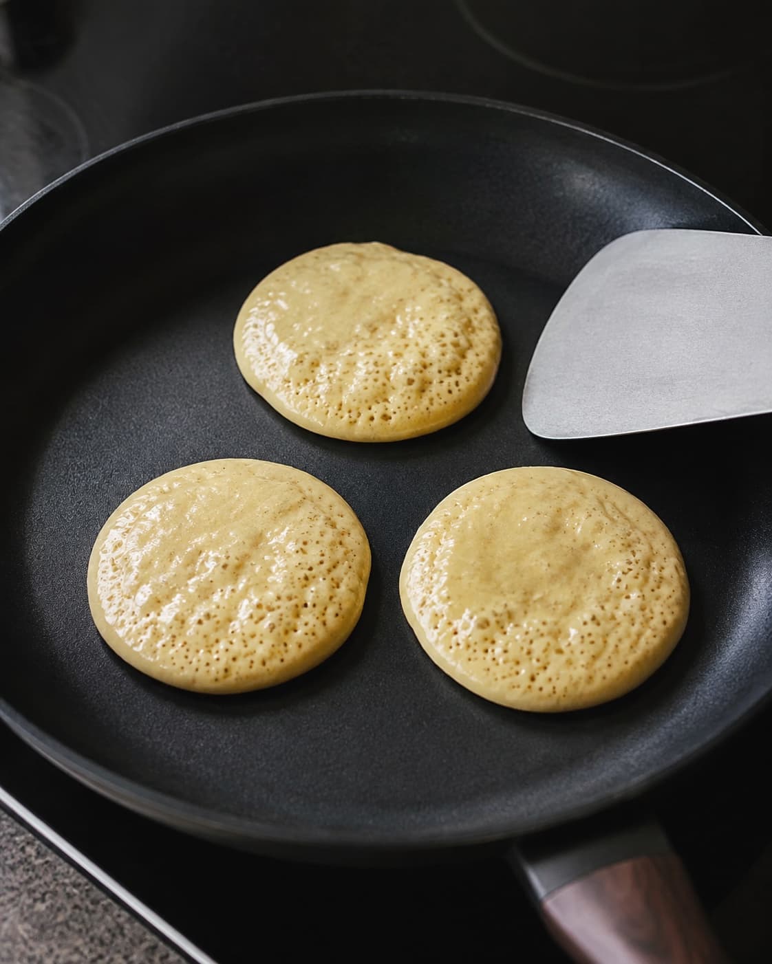 Tre små brunchpandekager med bobler og matte kanter er klar til at blive vendt én gang