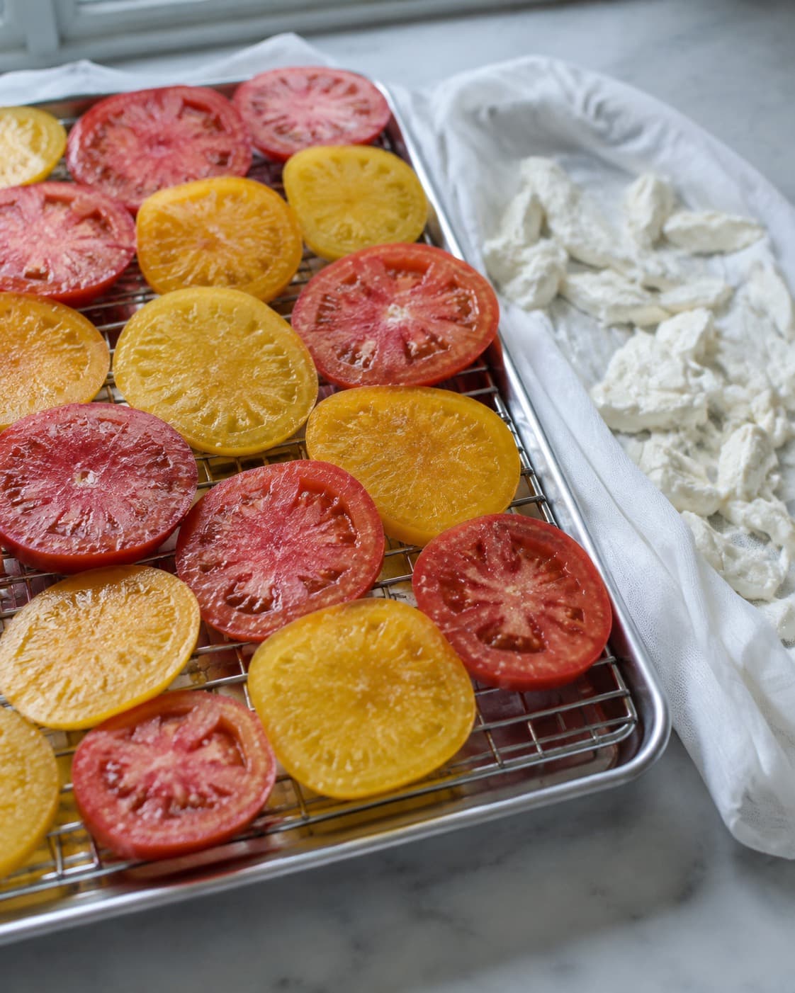 Tomatskiver saltes kort på rist, mens håndrevet mozzarella drypper af på klæde