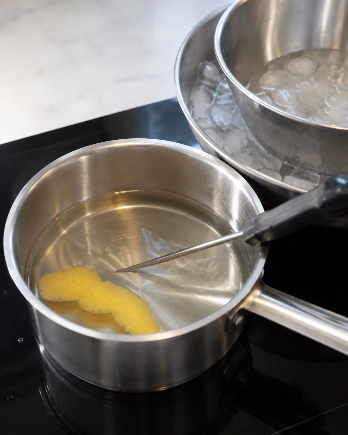Klar citronsirup måles med termometer ved siden af en metalskål i isbad