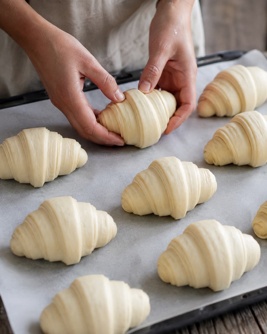 Formede croissanter med synlige lag hæver på bagepapir og spidserne ligger under bunden