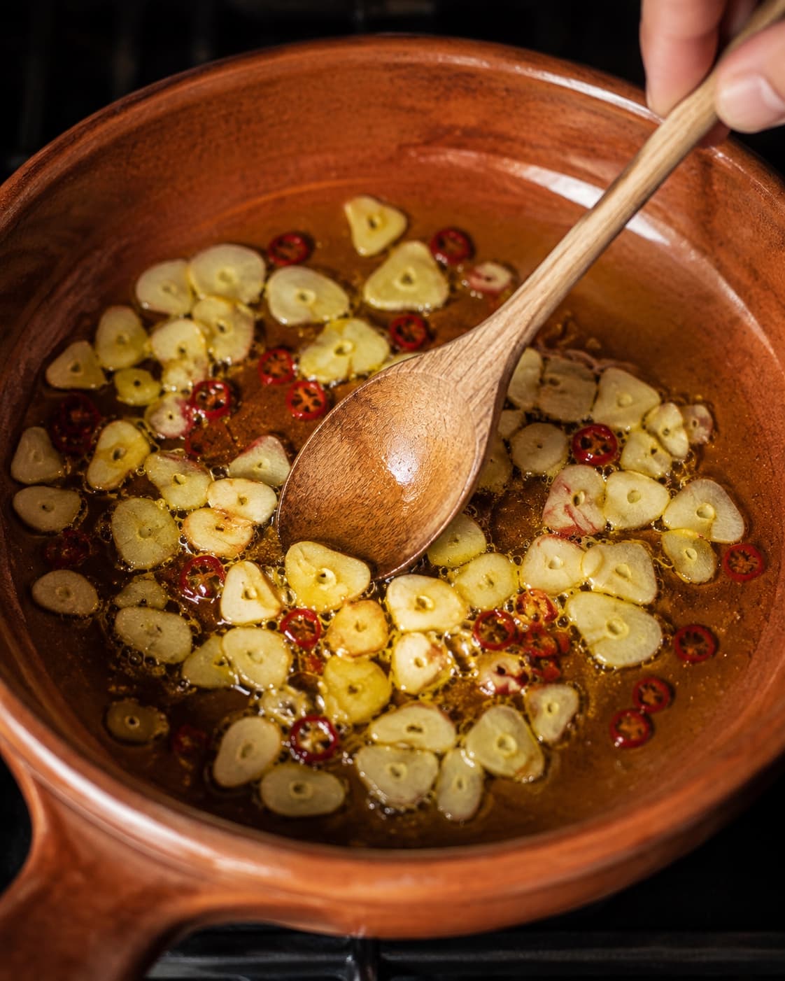 Tynde hvidløgsskiver bliver langsomt lyst gyldne i olivenolie med chili