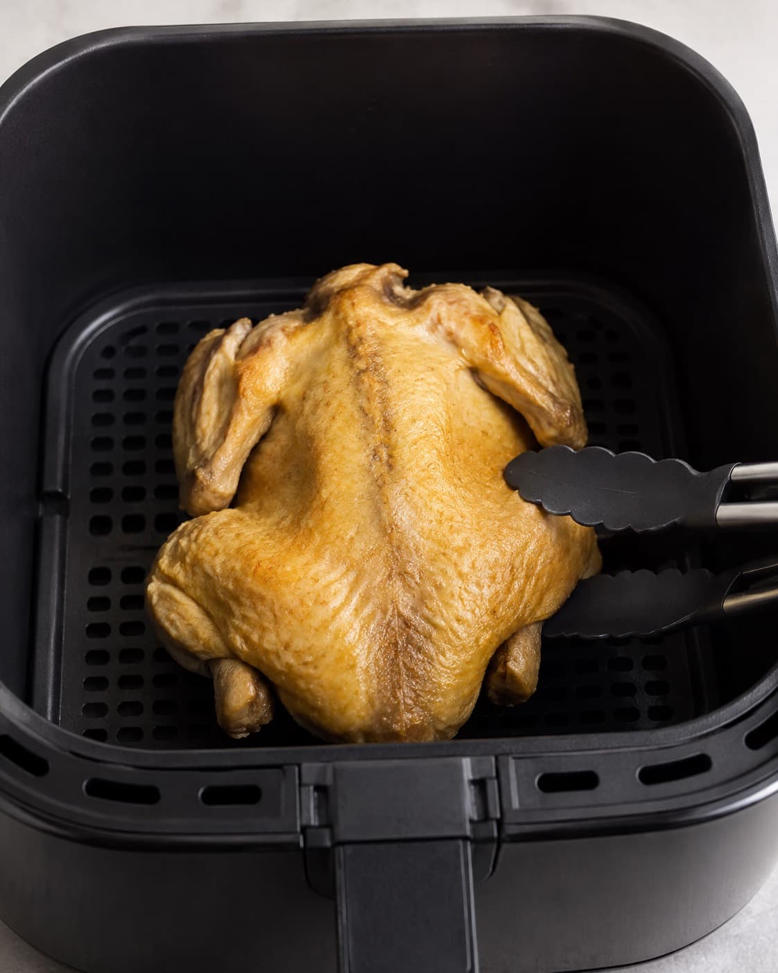 Kylling ligger brystside ned og rygside op i airfryer før én kontrolleret vending