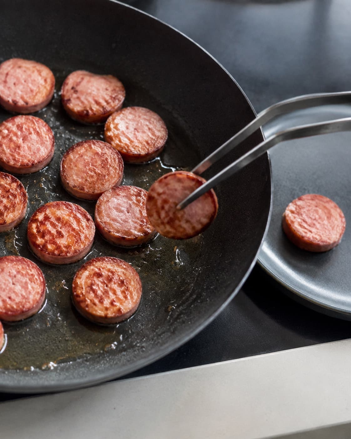 Pølseskiver brunes i ét lag og flyttes til et rent fad